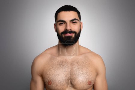 Foto de Estudio de toma de guapo morena barbudo árabe hombre posando sin camisa sobre fondo gris, sonriendo a la cámara, mostrando bonito cuerpo atlético después de la ducha - Imagen libre de derechos