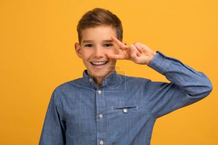 Photo for Portrait of joyful teen boy showing peace gesture at camera, cheerful happy teenage male child gesturing v-sign with hand while posing isolated on yellow studio background, copy space - Royalty Free Image
