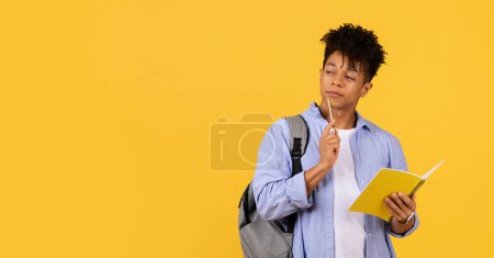 Photo for Contemplative black male student with backpack holding pencil to his chin and notebook, lost in thought against yellow background, embodying focus and academic curiosity - Royalty Free Image