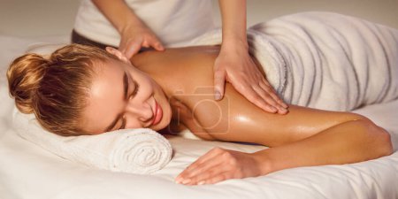 Photo for Woman enjoying shoulder massage in the health spa, lying with closed eyes - Royalty Free Image