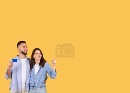 Photo for Happy couple looking upwards with excitement, man presenting credit card while lady pointing at free space, suggesting ideas for spending or investment opportunities - Royalty Free Image