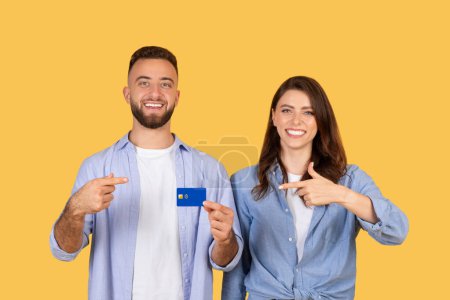 Pareja joven sonriente apuntando con confianza a la tarjeta de crédito azul, que representa decisiones financieras inteligentes y la conveniencia de transacciones sin efectivo