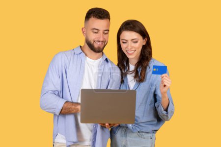 Photo for Happy young couple engaged in online shopping, with man holding laptop and woman showing credit card, symbolizing ease of digital transactions - Royalty Free Image