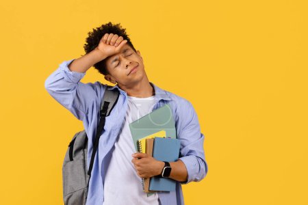 Black student guy clutching notebooks and looking overwhelmed, wipes his forehead, signaling stress or fatigue, set against bright yellow background, free space