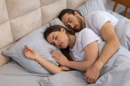 Téléchargez les photos : Couple repose dans un sommeil serein, partageant le confort d'un lit doux avec des expressions douces, illustrant des moments intimes de repos et de convivialité - en image libre de droit