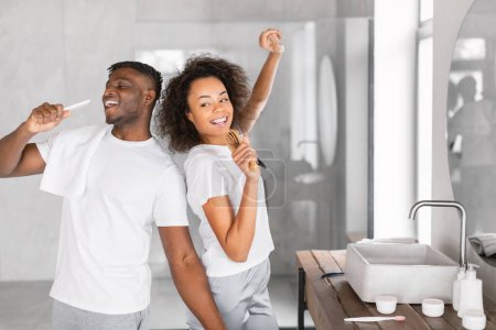 Photo for Young black couple engages in tooth brushing singing during happy and carefree morning routine, caring for teeth cleanliness and having fun in modern bathroom. Free space for text - Royalty Free Image