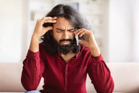 Photo for Upset bearded millennial indian man have phone conversation with girlfriend, touching head, talking about breakup. Eastern guy have bad news, talking on smartphone, closeup, copy space - Royalty Free Image