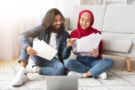 Photo for Happy young muslim couple checking documents while sitting on floor at home, smiling arabic spouses looking financial papers, reading insurance agreement or planning family budget, free space - Royalty Free Image