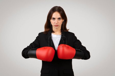Photo for Determined caucasian millennial professional woman with a focused gaze wearing red boxing gloves, symbolizing empowerment and readiness to tackle challenges in the business arena - Royalty Free Image