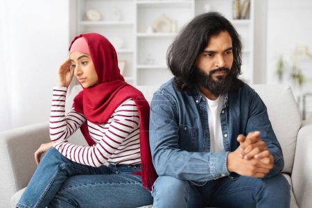 Besorgtes muslimisches Paar, das nach einem Streit auf dem Sofa sitzt, junge arabische Ehepartner, die emotionale Distanz und zwischenmenschliche Konflikte zeigen, Beziehungsprobleme haben, Nahaufnahme