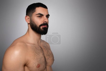 Téléchargez les photos : Homme concept de soins de la peau. attrayant sexy mi-nu athlétique barbu Moyen-Orient homme posant sur fond de studio gris, en regardant l'espace de copie pour la publicité - en image libre de droit