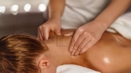 Téléchargez les photos : Masseur faisant massage du cou thérapeutique pour fille dans le spa avec éclairage sombre, gros plan - en image libre de droit