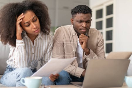 Photo for Money troubles. Frowning African American married couple using laptop doing paperwork, working with bills and budgeting, facing challenges in their lifestyle, dealing with financial issues at home - Royalty Free Image