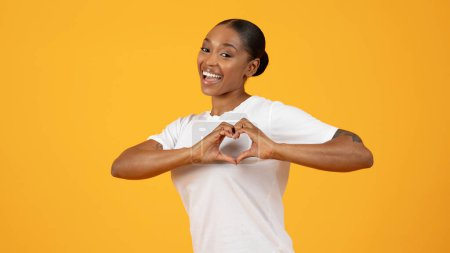Téléchargez les photos : Femme afro-américaine millénaire formant un cœur en forme de doigts, debout sur un fond jaune vif, montrant un symbole d'amour, de gratitude et de gentillesse. Panorama - en image libre de droit