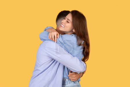 Affectionate young woman lovingly embraces her partner, eyes closed in contentment, against warm yellow background, symbolizing intimacy and joy