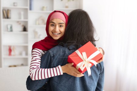 Téléchargez les photos : Portrait de heureuse femme musulmane agréable reçu cadeau romantique de son mari, femme reconnaissante tenant boîte cadeau et embrasser son conjoint, couple islamique célébrant la Saint-Valentin - en image libre de droit