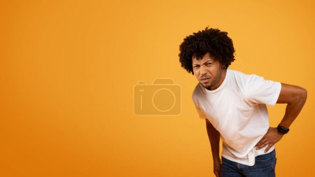 Ungesunder afrikanisch-amerikanischer lockiger Millennial-Mann, der seine Bauchseite berührt, unter Bauchschmerzen leidet, Nierenkolik hat, orangefarbener Hintergrund, Panorama mit Kopierraum