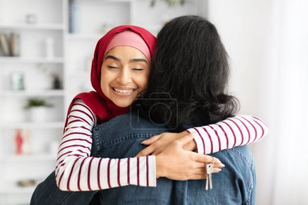 Foto de Mujer musulmana feliz abrazando al marido y sosteniendo las llaves de casa en la mano, cónyuges árabes celebrando el día de mudanza, abrazando en su nueva casa después de la reubicación, primer plano con enfoque selectivo - Imagen libre de derechos