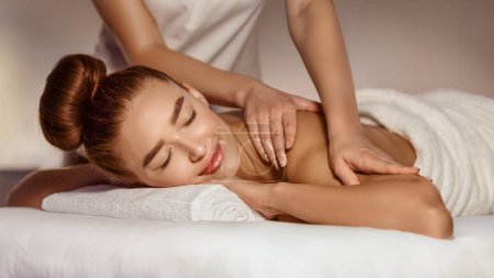 Téléchargez les photos : Soins du corps. Femme bénéficiant d'un massage des épaules avec les yeux fermés, allongé dans le salon de spa - en image libre de droit