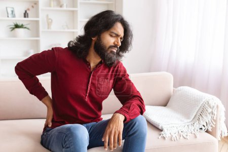 Photo for Upset millennial indian man feel sudden back pain muscles ache tension injury sitting at home, sad guy touching spine having lumbago backache osteoarthritis arthritis, backache concept, copy space - Royalty Free Image