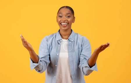 Photo for Portrait of cheerful black lady offering great deal smiling to camera and gesturing with hands, against yellow background. studio portrait shot. Concept of commercial promo - Royalty Free Image