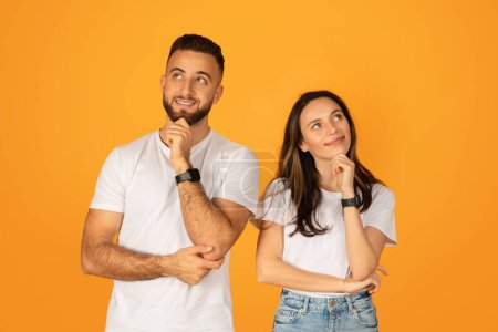 Photo for Contemplative young man and woman in white t-shirts, with hands on chin, looking upwards thoughtfully, possibly brainstorming or daydreaming, against a solid orange background - Royalty Free Image