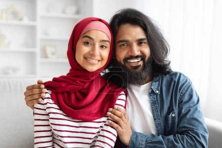 Téléchargez les photos : Gros plan d'un couple musulman heureux posant à l'intérieur de la maison, des conjoints arabes romantiques présentant des expressions joyeuses, embrassant et souriant à la caméra, profitant du confort domestique, espace libre - en image libre de droit