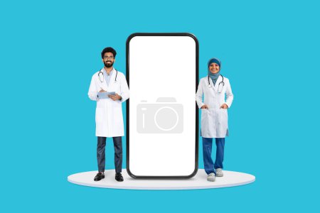 Ärztinnen und Ärzte stehen selbstbewusst neben dem aufragenden Smartphone-Bildschirm, ideal für Telemedizin-Dienste, auf blauem Hintergrund, Attrappe
