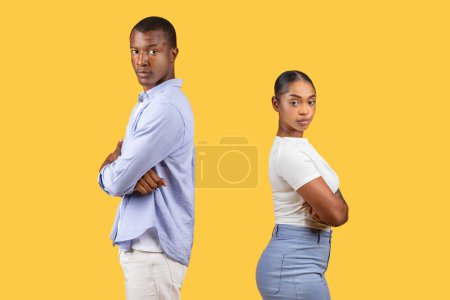 Black man and woman exhibit determination and confidence, standing back-to-back with arms folded, against vibrant yellow background, symbolizing strength and independence