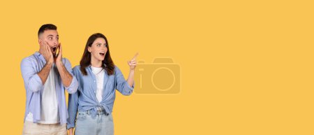 Téléchargez les photos : Homme étonné avec les mains sur les joues et femme excitée pointant quelque chose à l'espace libre, les deux montrant de grandes expressions sur fond jaune, panorama - en image libre de droit