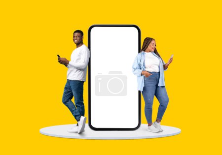 Smiling black man and woman engrossed in their smartphones beside an immense blank screen, symbolizing mobile connectivity on vivid yellow backdrop