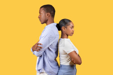 Schwarze Männer und Frauen stehen Rücken an Rücken mit verschränkten Armen und ernsten Gesichtsausdrücken, die vor schlichtem gelben Hintergrund auf Meinungsverschiedenheiten oder Patt hindeuten.