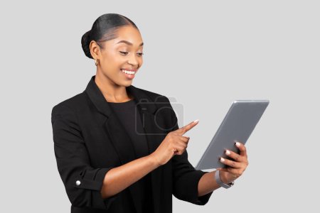 Téléchargez les photos : Joyeux millénariste dame noire en costume professionnel utiliser tablette, doigt pointant, isolé sur fond gris studio. Travail, application professionnelle, appareil, chat et mode de vie de présentation, démarrage - en image libre de droit