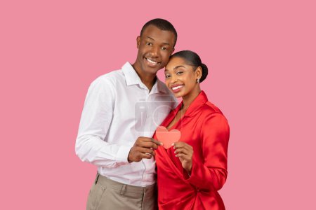 Photo for Happy black couple in elegant attire, man in white shirt and woman in red dress, smiling as they hold red heart together, symbolizing love and togetherness - Royalty Free Image