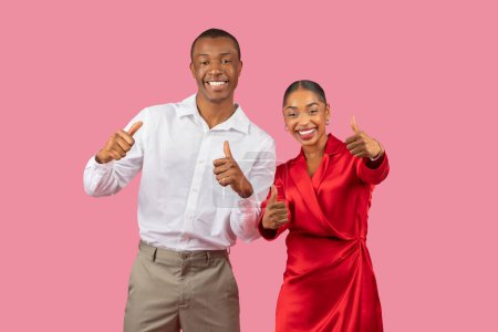Téléchargez les photos : Rayonnant jeune homme et femme noirs dans des vêtements élégants donnant joyeusement pouces à la caméra, signifiant l'approbation et la positivité sur fond rose - en image libre de droit