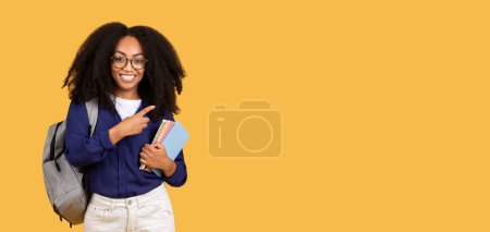 Photo for Joyful black lady student carrying backpack and copybooks points to free space, on yellow background, symbolizing potential and opportunity in the realm of education - Royalty Free Image
