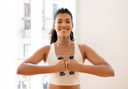 Photo for Portrait of happy fitness lady in fitwear holding dumbbells in front of chest, working out at home, smiling to camera. Bodybuilding exercises and healthy lifestyle concept - Royalty Free Image