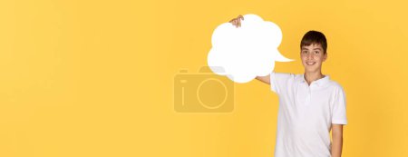 Foto de Un joven sonriente con una camisa de polo blanca sostiene con confianza un recorte de burbujas en blanco, invitando a la conversación o las ideas, sobre un fondo amarillo brillante, panorama - Imagen libre de derechos