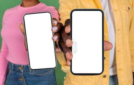 Photo for Man and woman hands showing two brand new modern gadgets cell phones with white empty screen, isolated on green studio background. Black couple recommending nice mobile app or online offer, deal - Royalty Free Image