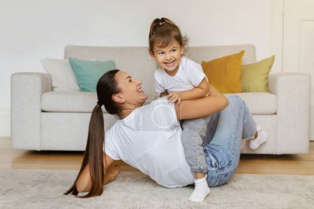 Photo for Cheerful mother playing with her little daughter in living room, happy family of two mom and preschool female child enjoying a fun moment together at home, bonding and laughing, copy space - Royalty Free Image