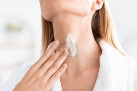 Photo for Cropped shot of blonde lady applying moisturizer on neck skin, enhancing smoothness with beauty product, enjoying skincare ritual and luxury cosmetics, in bathroom indoors, closeup - Royalty Free Image