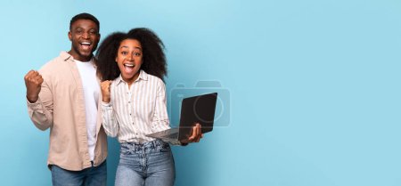 Photo for Overjoyed young black couple holding an open laptop, celebrating success with bright blue background expressing happiness and achievement, panorama with free space - Royalty Free Image