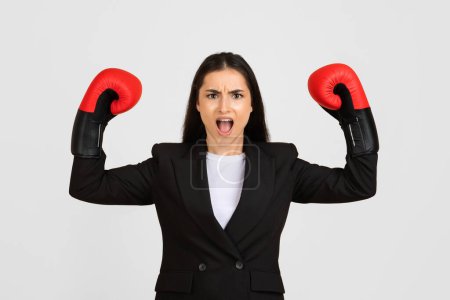 Photo for Fierce and empowered businesswoman wearing boxing gloves raises her fists in fighting stance, symbolizing challenge and strength in business - Royalty Free Image