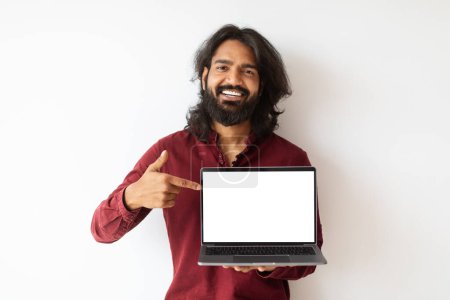 Photo for Cool cheerful bearded long-haired young indian man showing laptop computer with white blank screen mockup copy space, isolated on white wall background. Online education, e-learning - Royalty Free Image