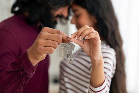 Photo for House Ownership. Loving Young Indian Couple Holding Showing Key Standing In New Flat, Emotional Guy And Lady Posing Cuddling After Moving In Own Apartment. Insurance, Real Estate, Mortgage Concept - Royalty Free Image