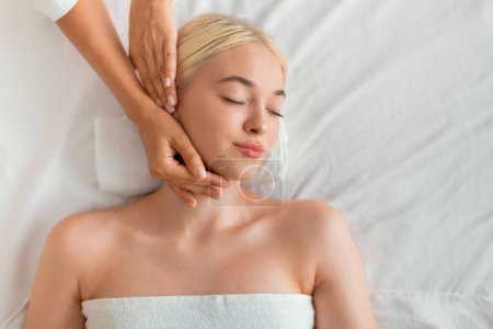 Top ansicht von jung blond europäisch dame genießen facebuilding massage drinnen. Frau erhält Gesichtsbehandlung, Porträtaufnahme von oben. Verwöhnung und Entspannung