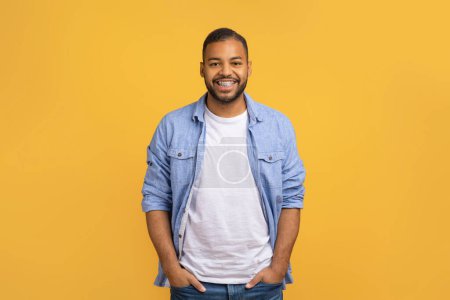 Photo for Handsome Young African American Man Holding Hands In Pockets While Standing Over Yellow Studio Background, Cheerful Black Male Smiling To Camera, Expressing Positive Emotions, Copy Space - Royalty Free Image