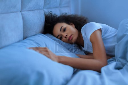 Photo for Depressed African American Woman After Divorce Touching Empty Pillow Lying In Bed Alone At Night. Woman Suffering From Loneliness Missing Her Partner In Bedroom After Breakup. Low Light - Royalty Free Image