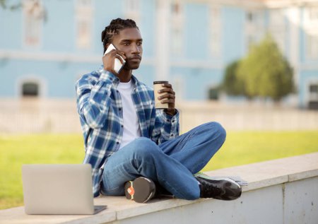 Photo for Calm black student guy talking on mobile phone sitting with laptop outside, holding paper coffee cup, studying online with computer at university campus outdoors on sunny day - Royalty Free Image