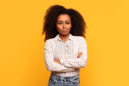 Photo for Skeptical young black lady with curly hair, arms crossed and dubious expression, standing against vibrant yellow background, looking at camera - Royalty Free Image